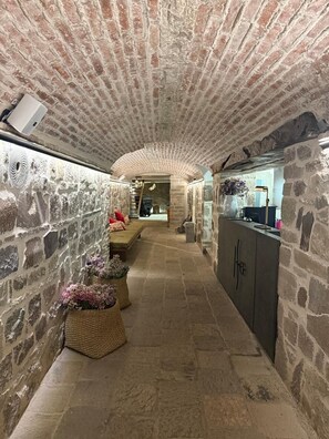 A stone-walled corridor with a bench, wicker baskets with flowers, and a reception desk.
