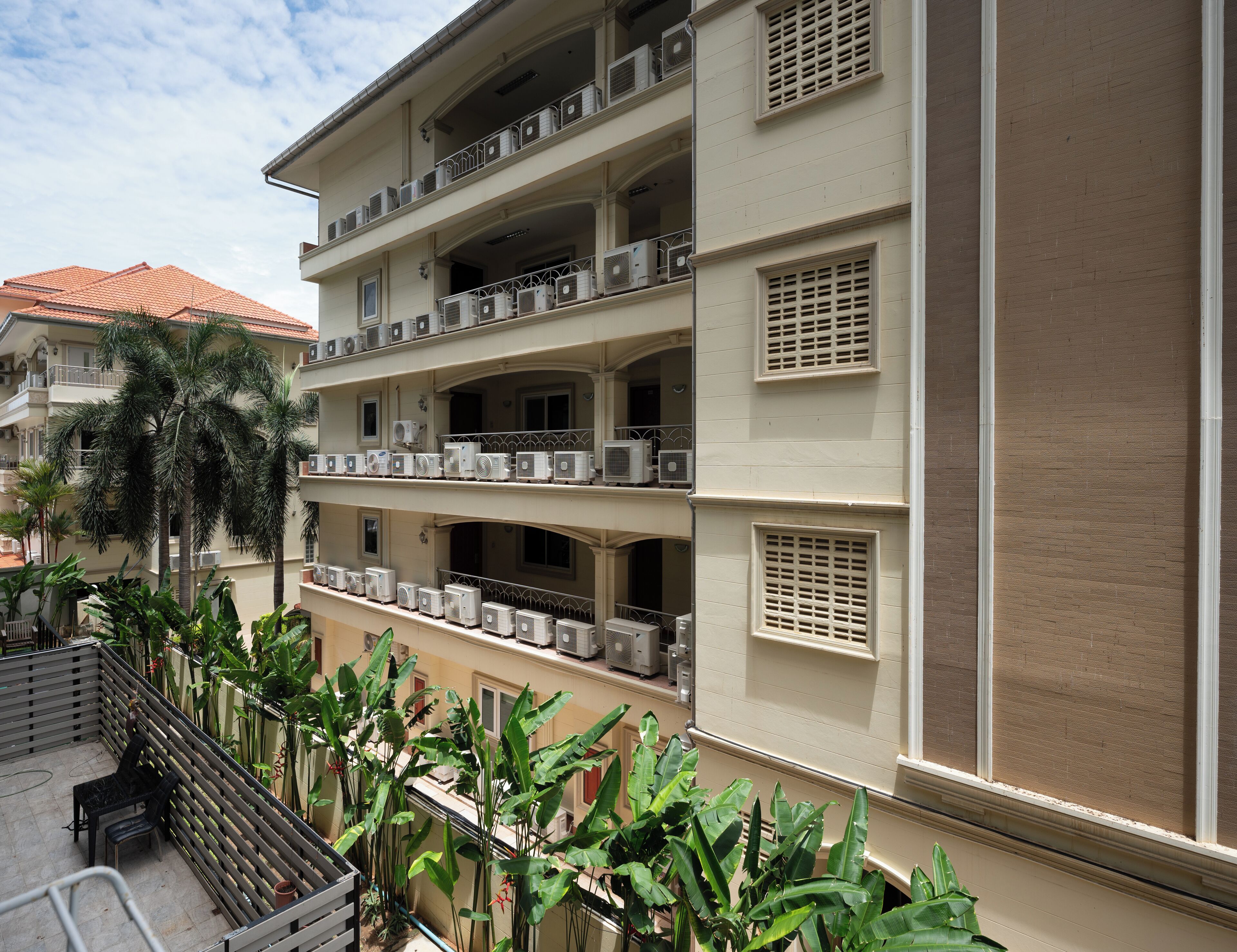 A multi-story hotel with balconies, air conditioning units, and lush greenery.