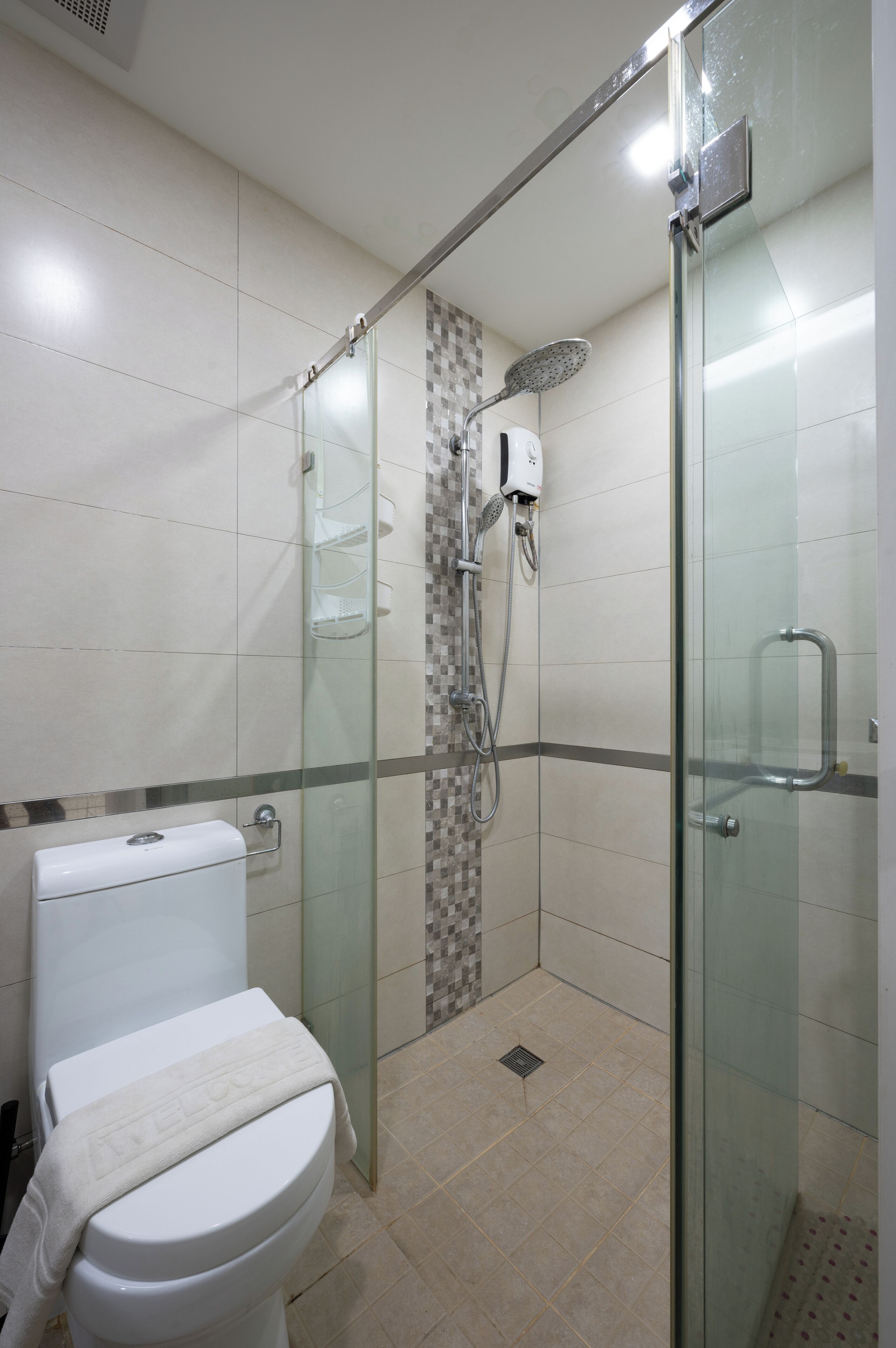 A modern bathroom with a glass-enclosed shower, a toilet with a towel, and a tiled floor.