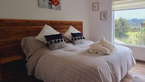 Un dormitorio con cabecera de madera, un ventanal con vistas y un cuadro de flores en la pared.