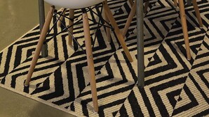 Un comedor con una mesa larga, sillas blancas, un tapete estampado y una planta.