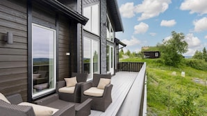 A modern house with a deck featuring wicker furniture and a view of a green landscape. - 4 Star Holiday Home in Fall (Søndre Land)