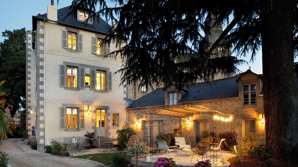 A two-story stone house with a covered patio, outdoor seating, and a well-maintained garden. - Clos du Cèdre (Dinan)