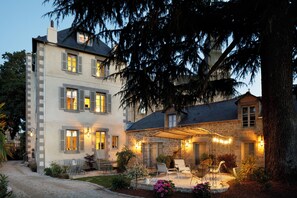 A two-story stone house with a covered patio, outdoor seating, and a well-maintained garden. - Clos du Cèdre (Dinan)