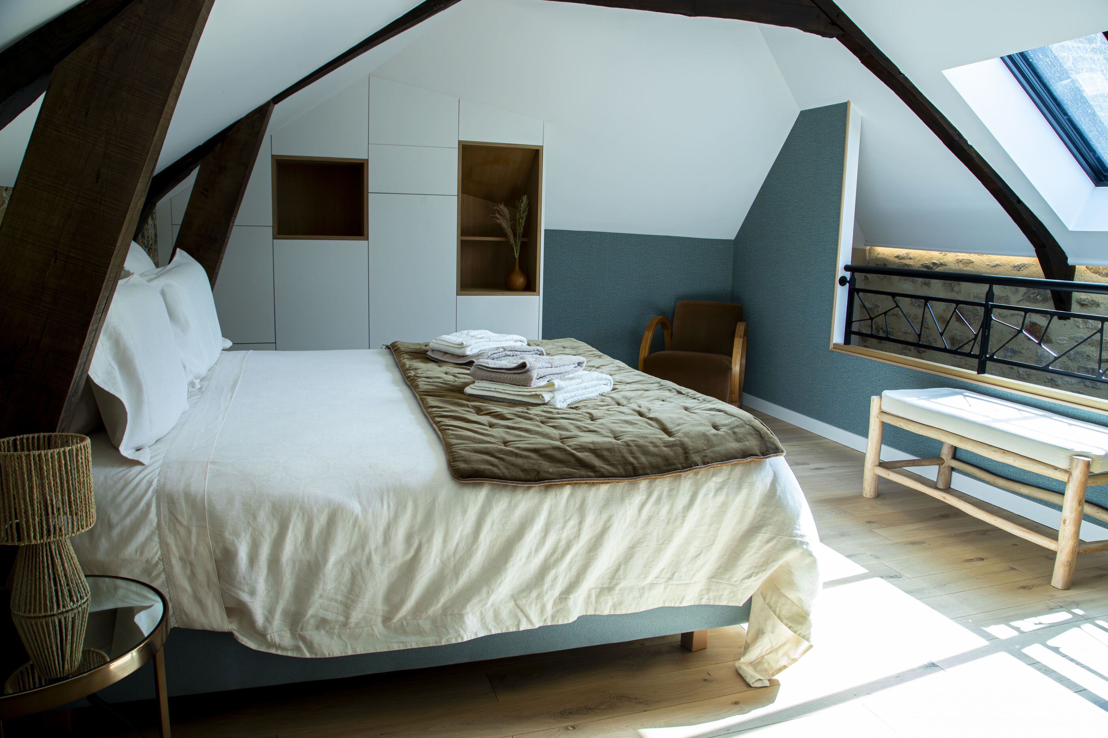 Un dormitorio con cama, mesita de noche, una silla, un pequeño estante y una ventana.