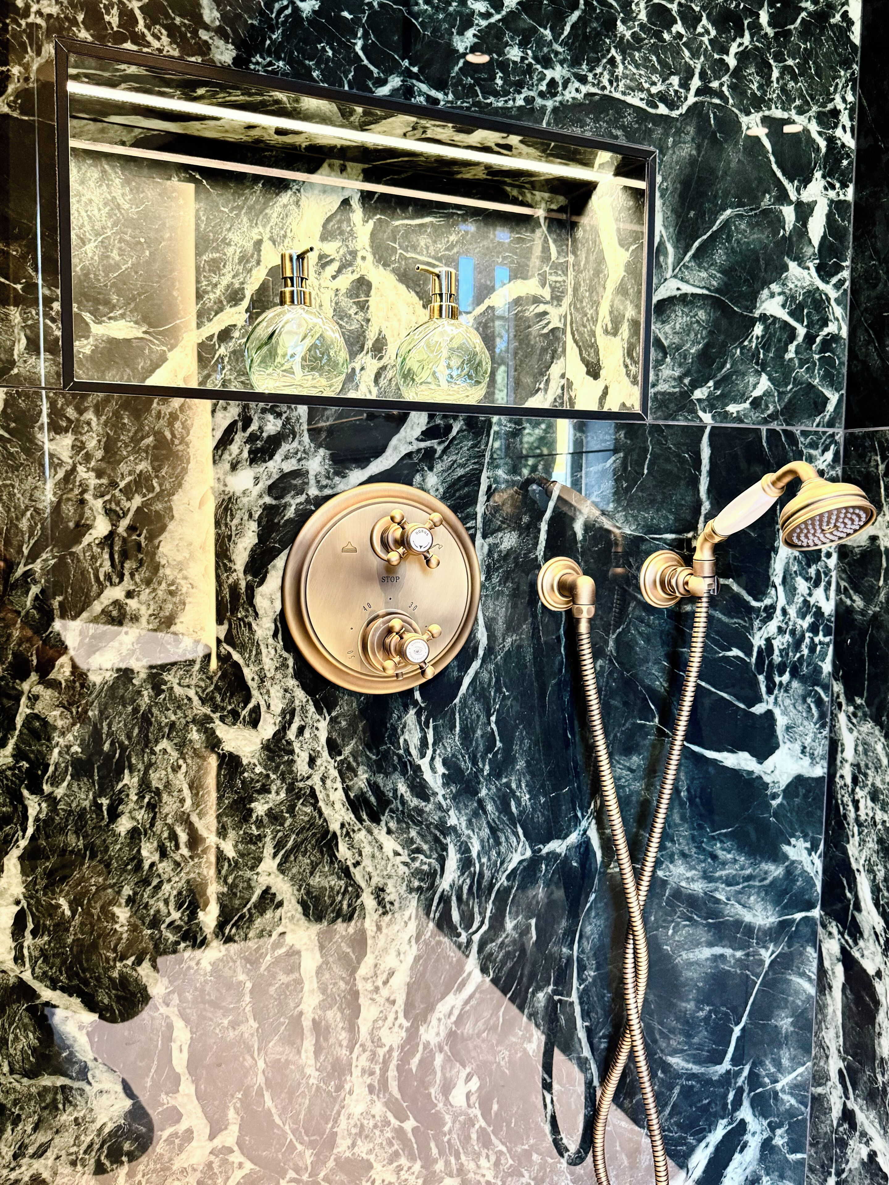 Ein Badezimmer mit Marmorboden, Brausekopf und Armatur in Gold.