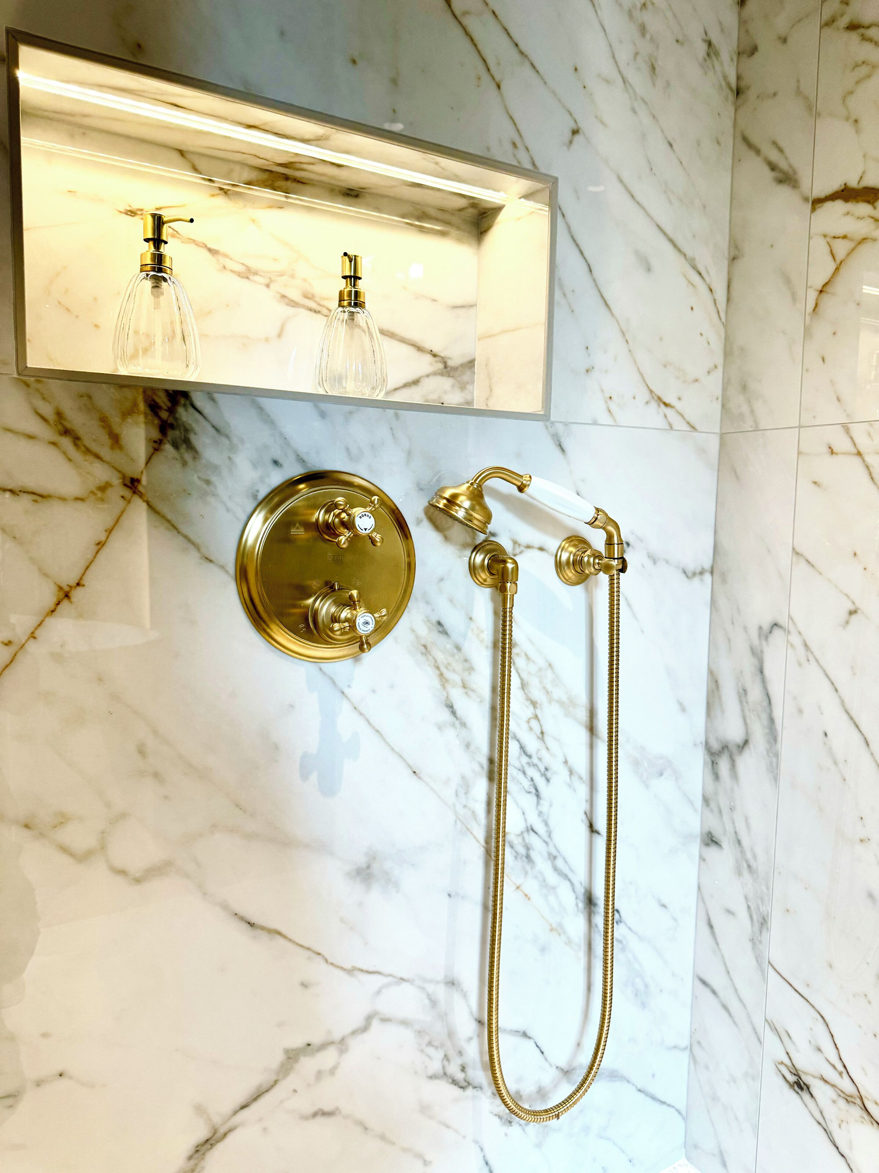 A bathroom with a marble floor, a gold showerhead, and a gold faucet.