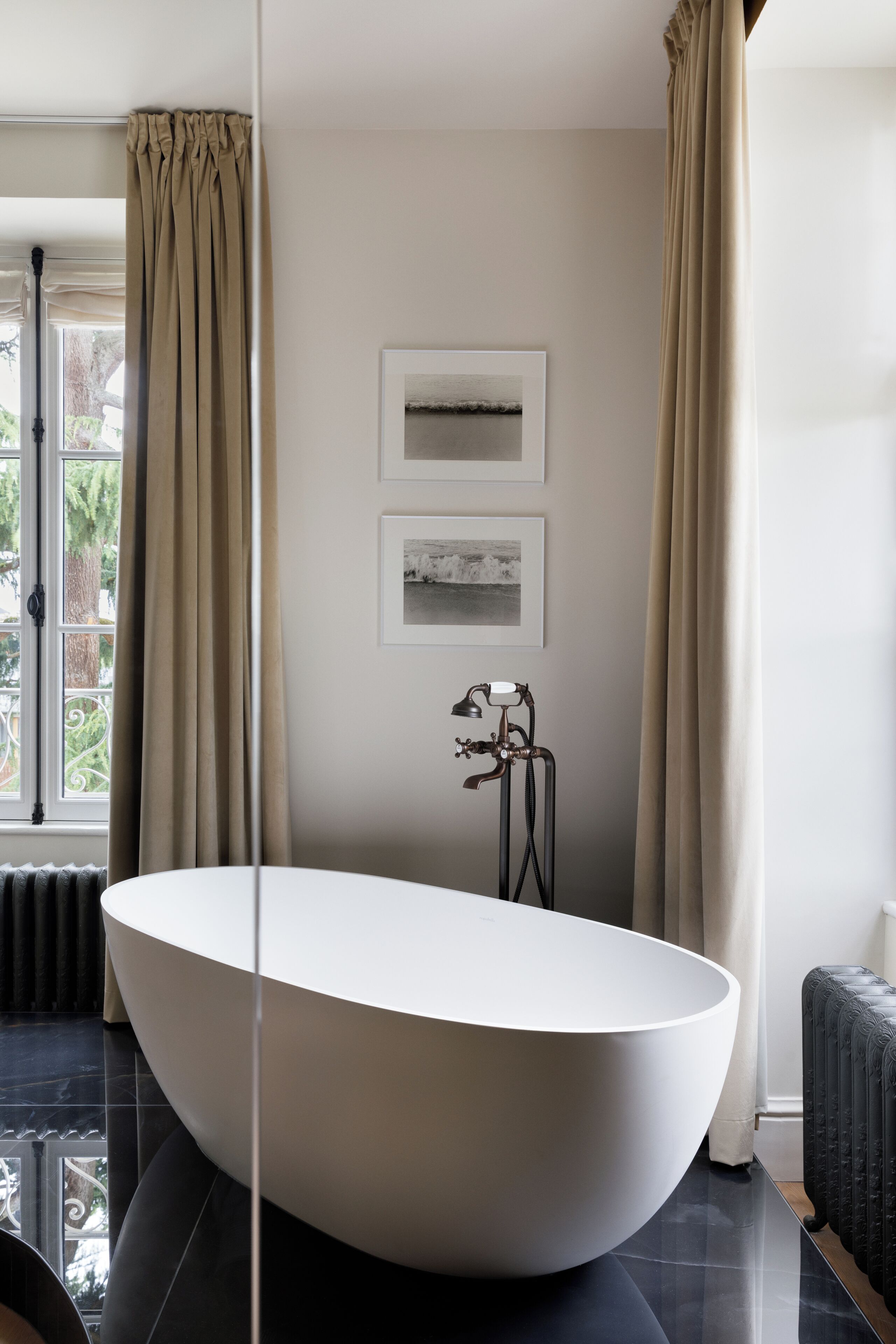 Un baño moderno con una bañera ovalada grande, un radiador y un ventanal con cortinas.