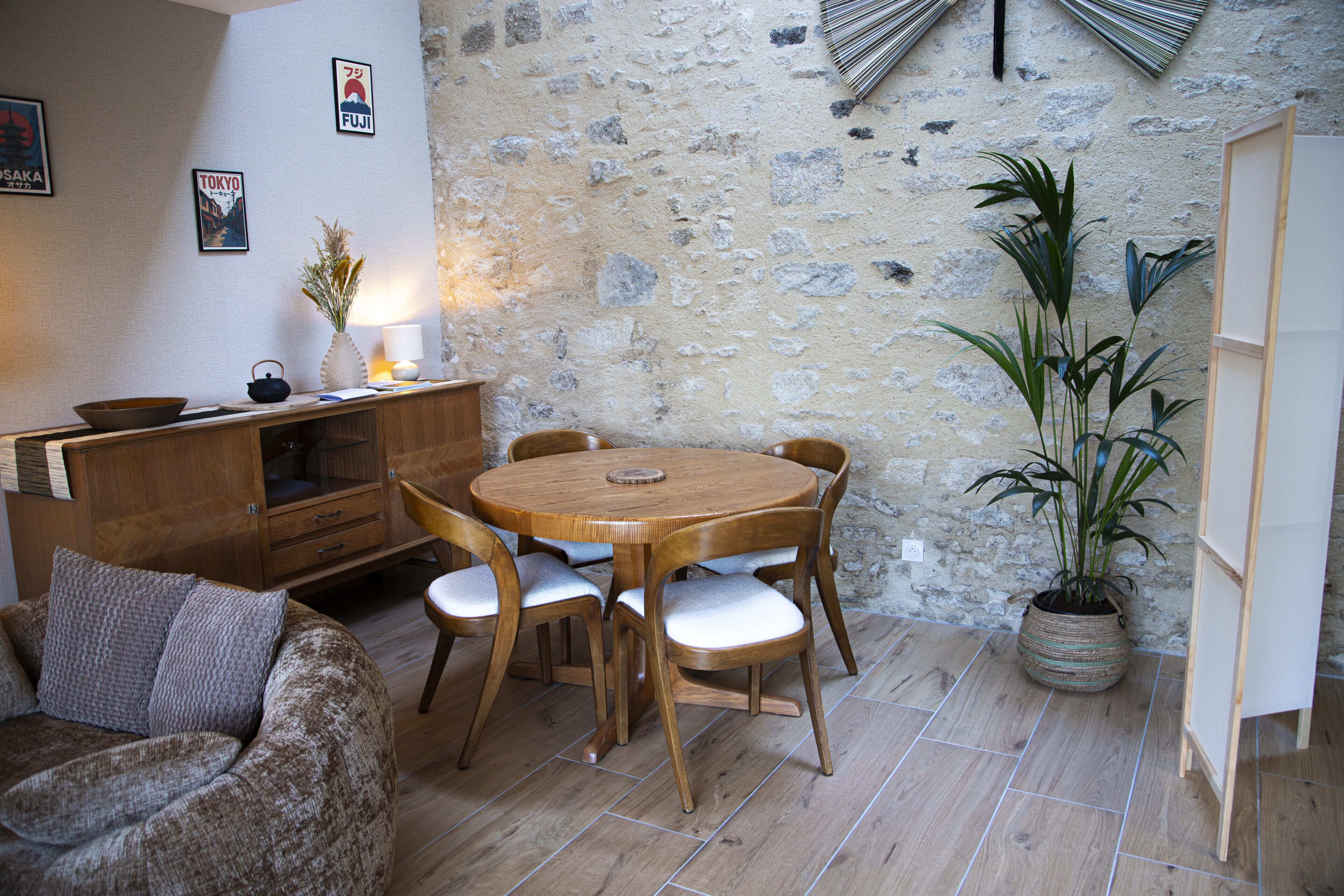 A cozy room with a round wooden table and chairs, a sofa, a potted plant, and a stone wall.
