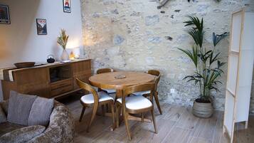 A cozy room with a round wooden table and chairs, a sofa, a potted plant, and a stone wall.