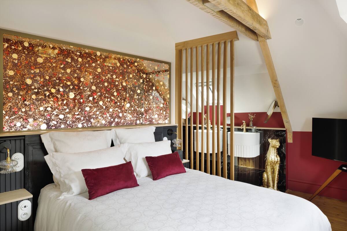 Quarto com cama grande, parede decorativa, divisória de madeira, cadeira vermelha e televisão.
