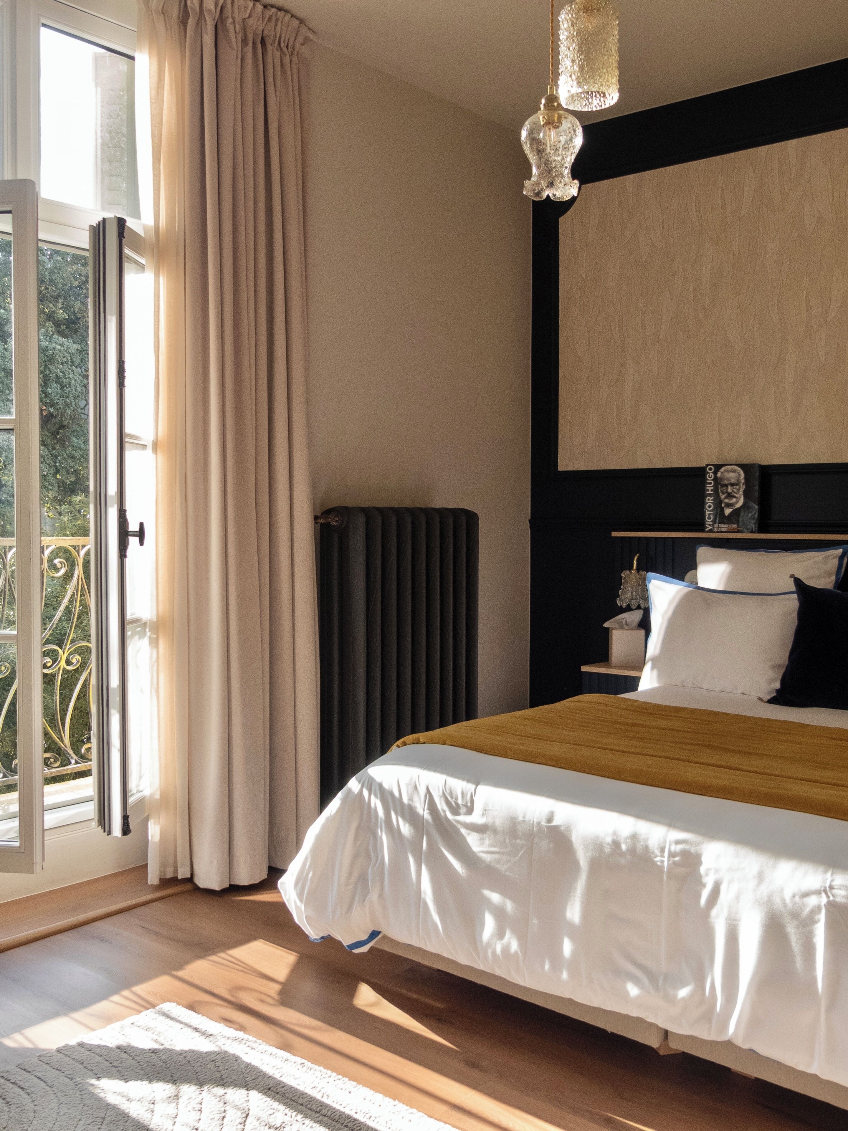 Une chambre avec un grand lit, un radiateur, une fenêtre avec des rideaux et une vue sur la verdure.