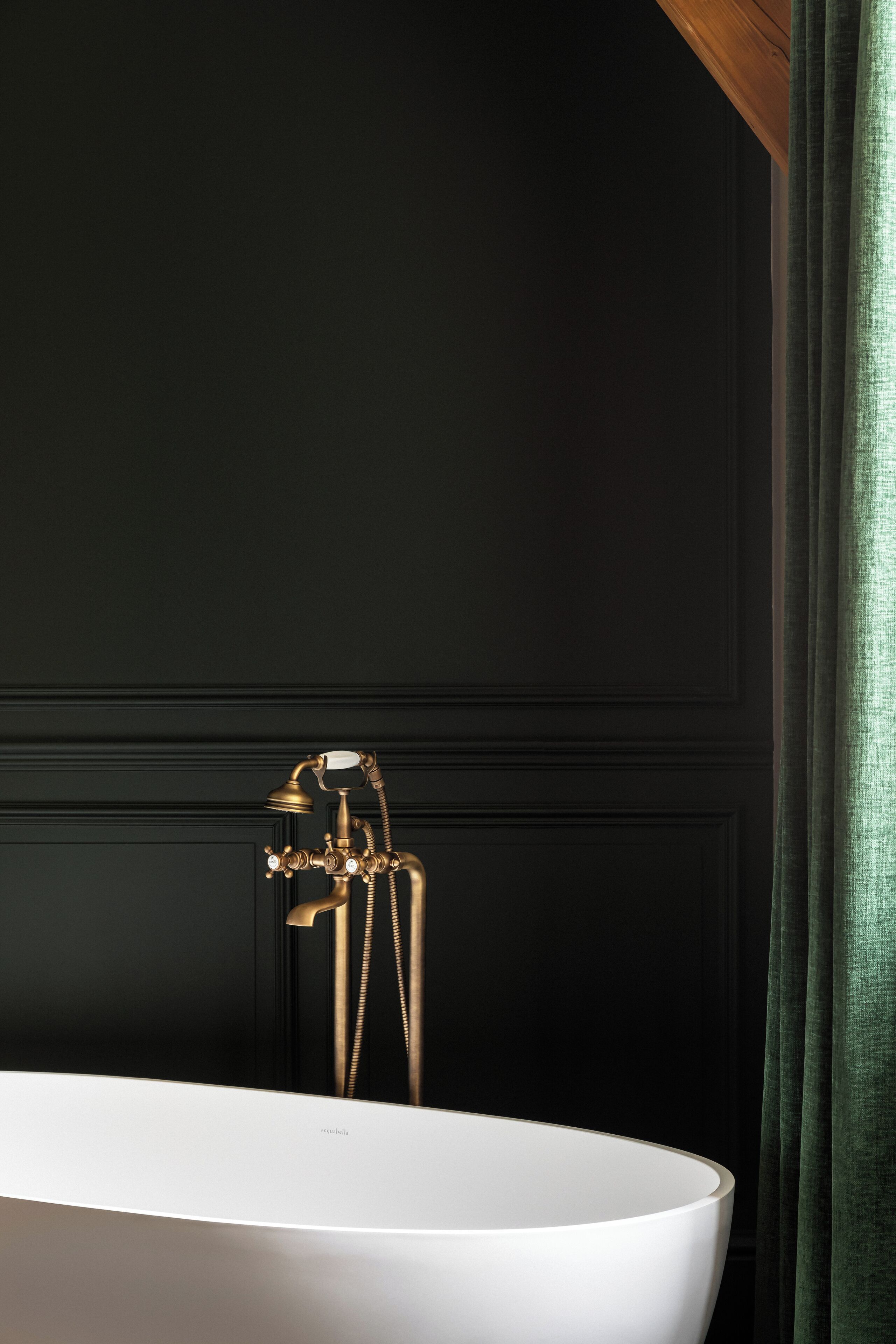 Eine weiße Badewanne mit goldenem Wasserhahn vor einer dunklen Wand.