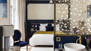 A modern hotel room with a large bed, a round white console table, a side table, a large mirror, and a white bench. - Clos du Cèdre (Dinan)