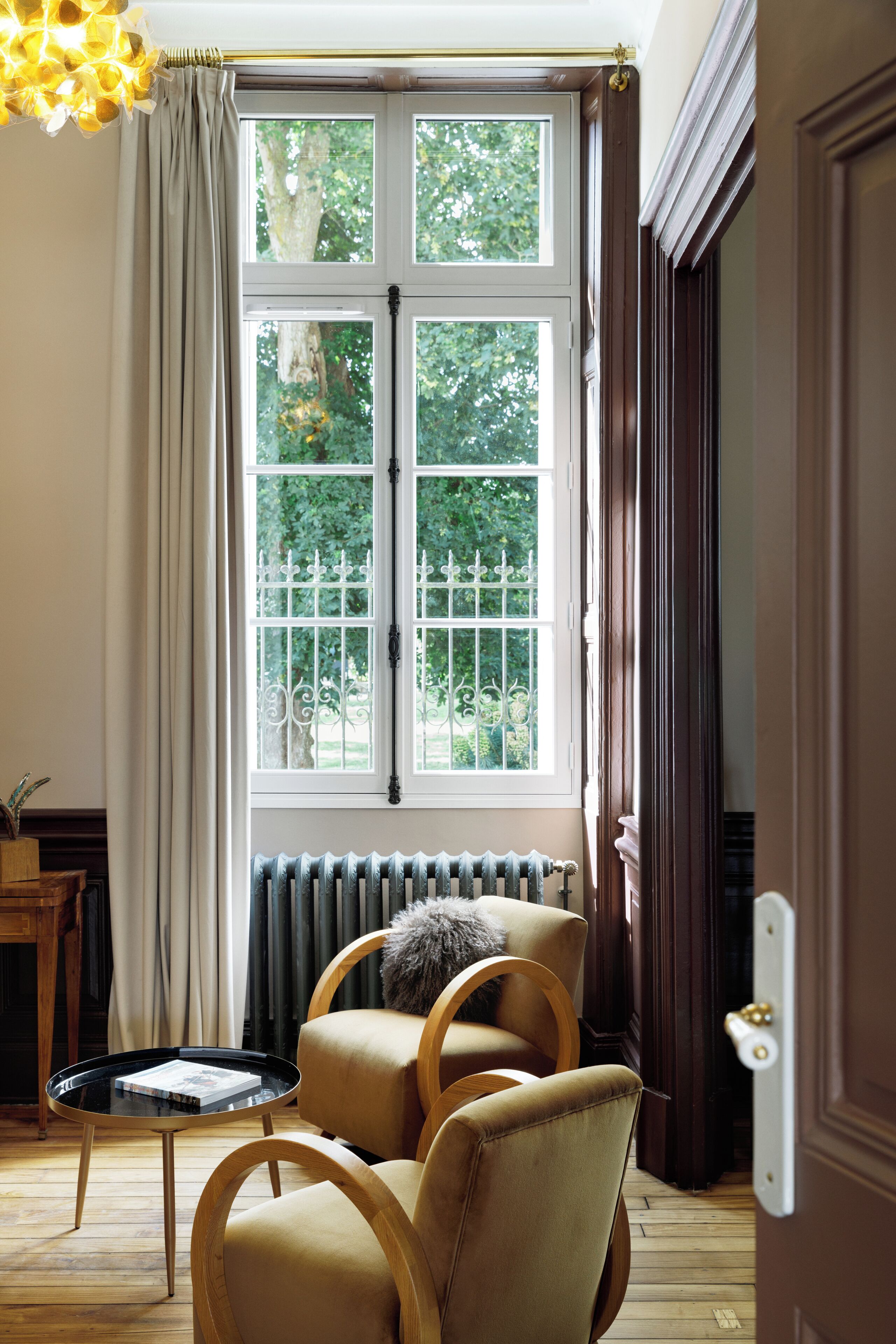 A room with a large window, a radiator, a wooden chair, and a small table with a book.