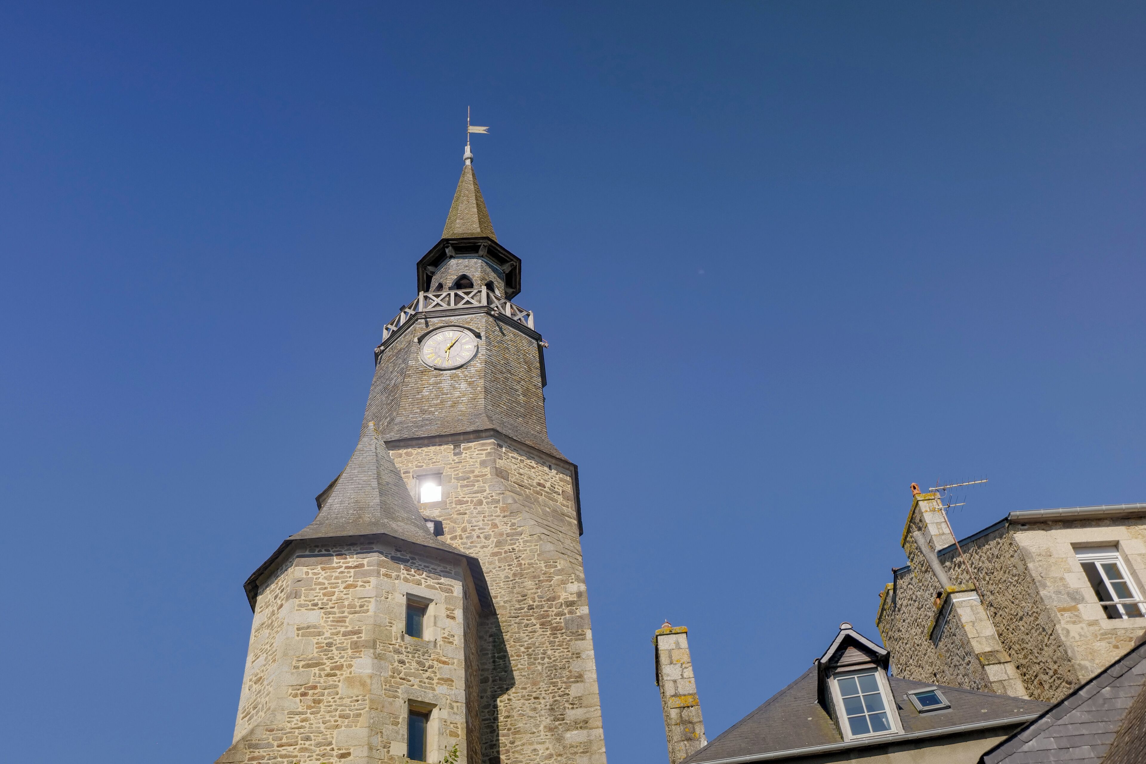 A tall stone tower with a clock and a flag on top.