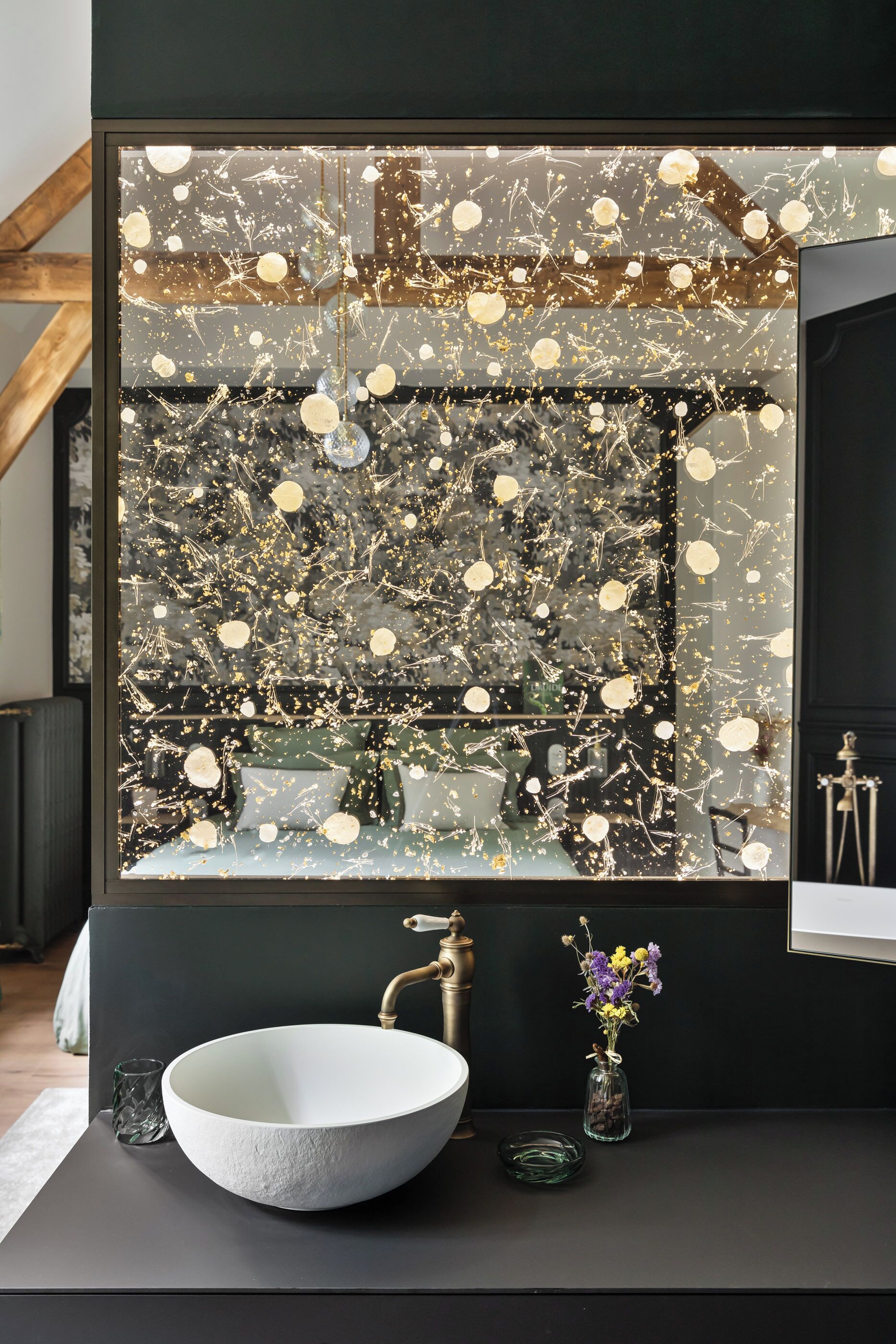 Une salle de bain moderne avec un grand miroir, un lavabo sur colonne blanc et un mur décoratif parsemé de paillettes dorées.