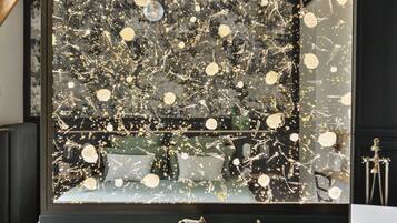 Une salle de bain moderne avec un grand miroir, un lavabo sur colonne blanc et un mur décoratif parsemé de paillettes dorées.