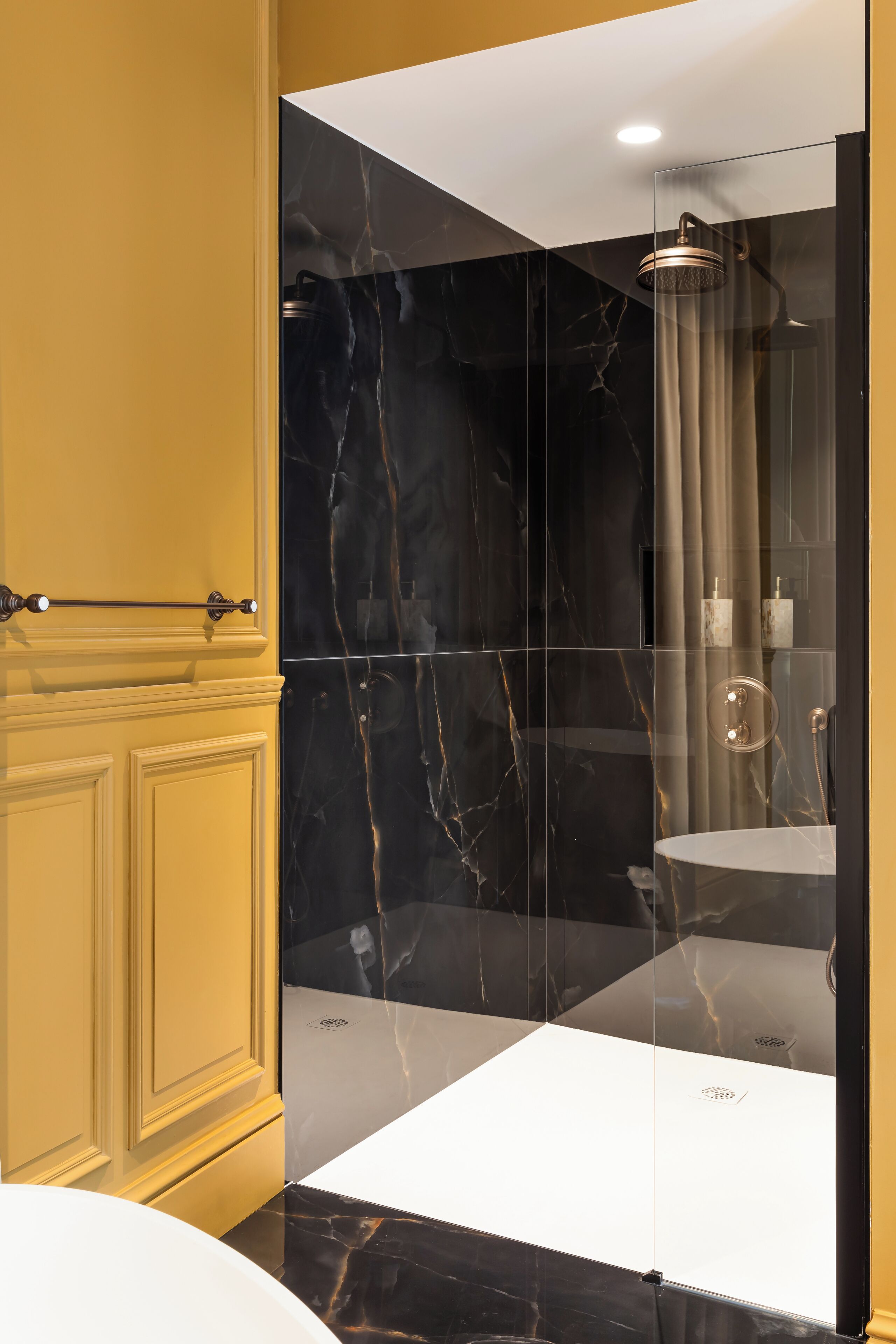 Een moderne badkamer met een douchecabine van glas, marmeren wanden en een wit wastafel.
