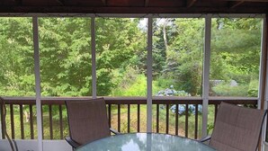 A glass-top table with two chairs on a wooden deck, overlooking a lush green landscape. - TreeFort, ZipLine, Kayaks, Beach6min drive, Vaulted Ceilings, ScreenPorch & Deck (Narragansett)