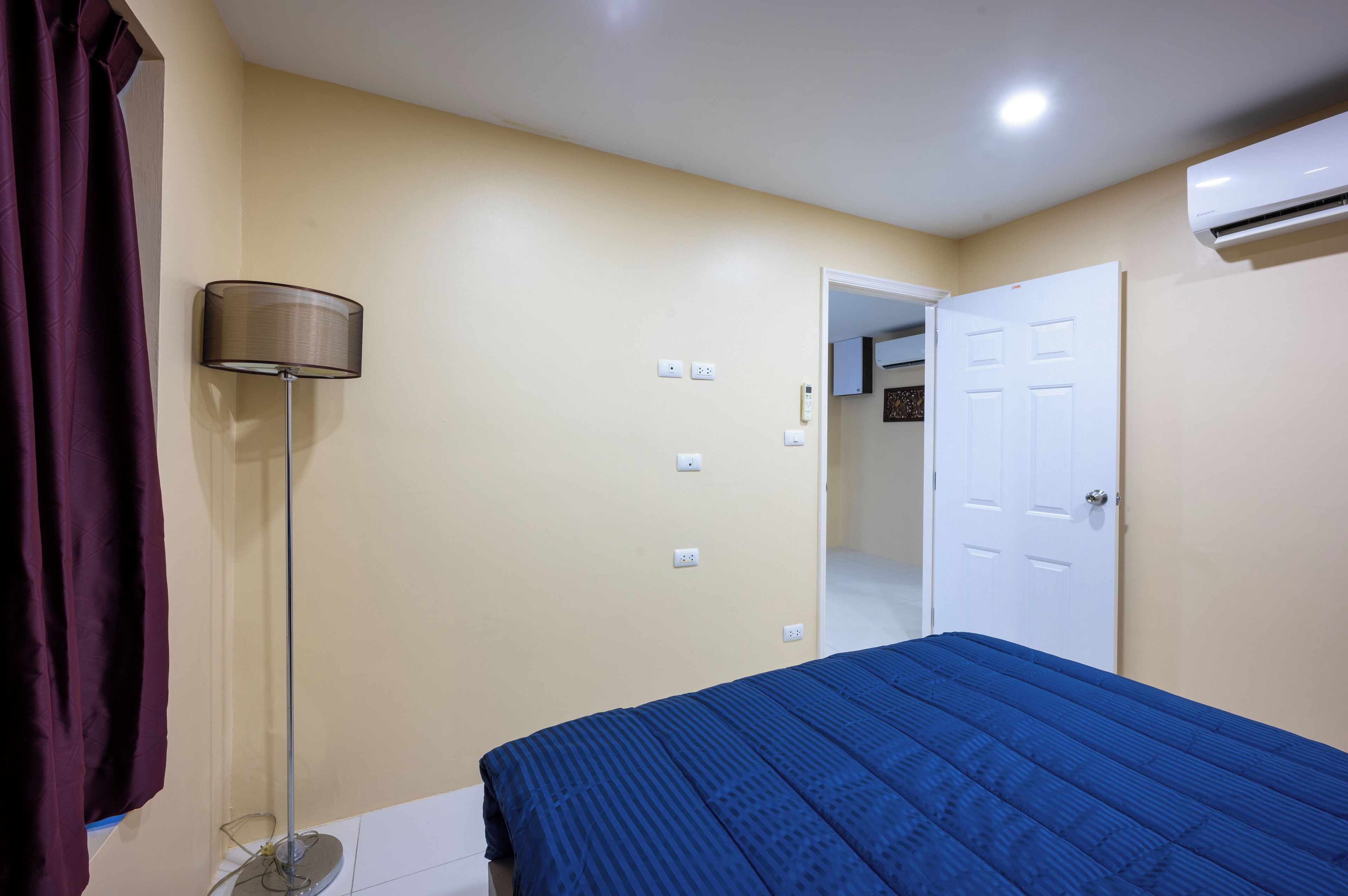Un dormitorio con una cama, una lámpara, aire acondicionado y una puerta.