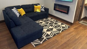A living room with a sectional sofa, a flat-screen TV, a fireplace, and a patterned rug. - Cozy Cabin with Stunning Views (Seward)