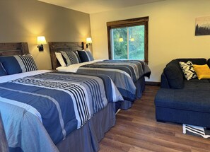 A hotel room with two beds, a sofa, and a window with a view of trees. - Cozy Cabin with Stunning Views (Seward)