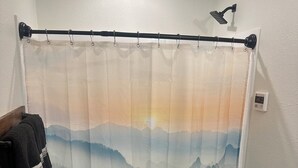 A bathroom with a shower curtain depicting a mountain landscape, a toilet, a sink, and a towel rack with a towel. - Cozy Cabin with Stunning Views (Seward)
