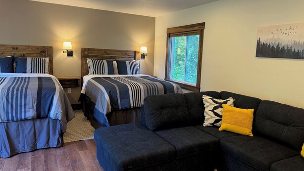 A hotel room with two beds, a sofa, and a window with a view of trees. - Cozy Cabin with Stunning Views (Seward)