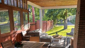 Een terras buiten met een houten tafel en bankjes, omgeven door een houten schutting en bomen.