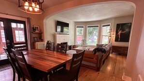Een eetruimte met een houten tafel en stoelen, een keuken met een televisie, en een woonkamer met een bank en een open haard.