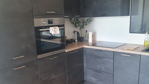 A modern kitchen with dark cabinetry, a herringbone wooden floor, and stainless steel appliances. - Refait à Neuf: 5min des Champs-elysees, La Defense Arena, 20min la Tour Eiffel (Neuilly-sur-Seine)