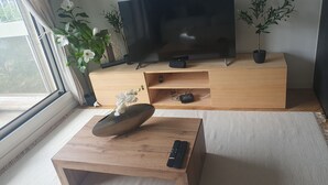 A modern living room with a flat-screen TV on a wooden stand, a coffee table with a vase of white flowers, and two potted plants. - Refait à Neuf: 5min des Champs-elysees, La Defense Arena, 20min la Tour Eiffel (Neuilly-sur-Seine)