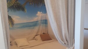 A bed with a beach scene backdrop, a hanging light fixture, and a rope tied to the curtain. - Refait à Neuf: 5min des Champs-elysees, La Defense Arena, 20min la Tour Eiffel (Neuilly-sur-Seine)