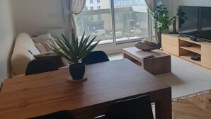 A modern living room with a sofa, a dining table, chairs, a TV, and a large window with curtains. - Refait à Neuf: 5min des Champs-elysees, La Defense Arena, 20min la Tour Eiffel (Neuilly-sur-Seine)
