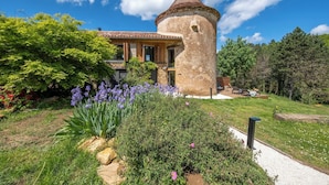 A stone tower with a conical roof, surrounded by lush greenery and flowering plants.
