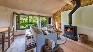 A cozy living room with a stone wall, a fireplace, and a large window offering a view of greenery.