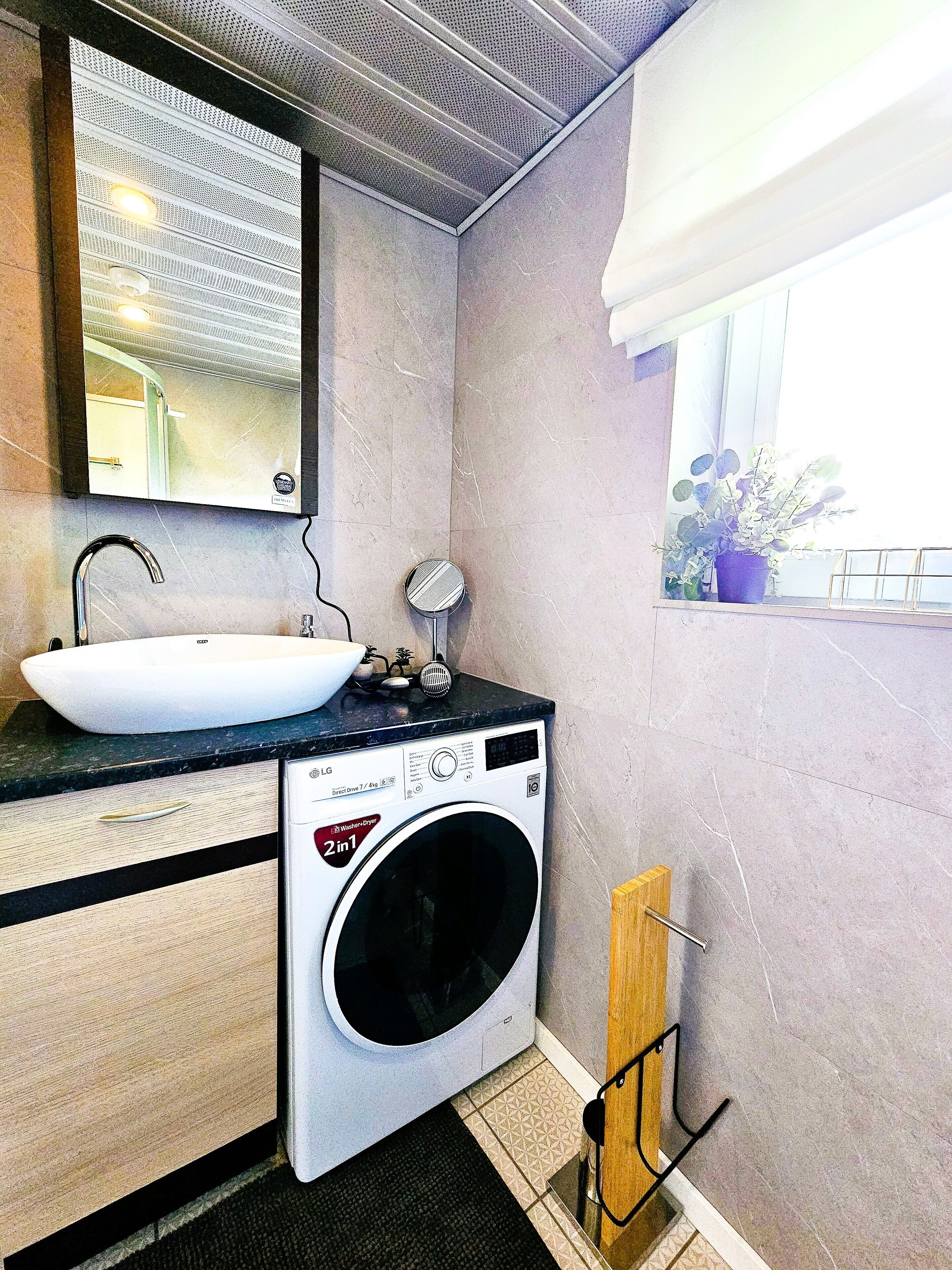 Ein kleines Badezimmer mit Waschbecken, Spiegel und Waschmaschine.