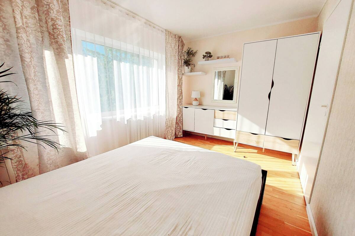 A bedroom with a bed, a dresser, a mirror, and a plant.