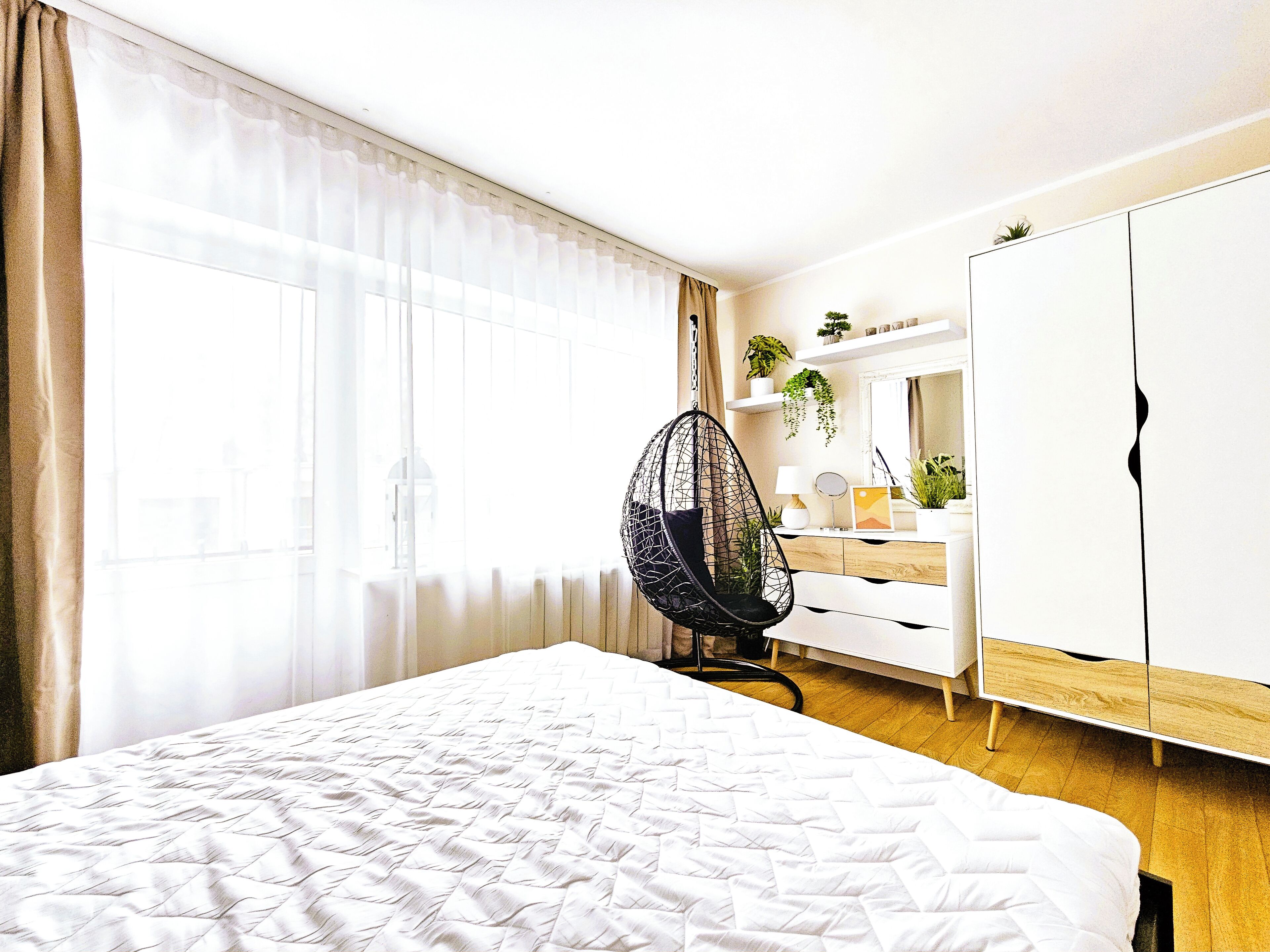 Een slaapkamer met een groot bed, een hangstoel, een dressoir en een spiegel.
