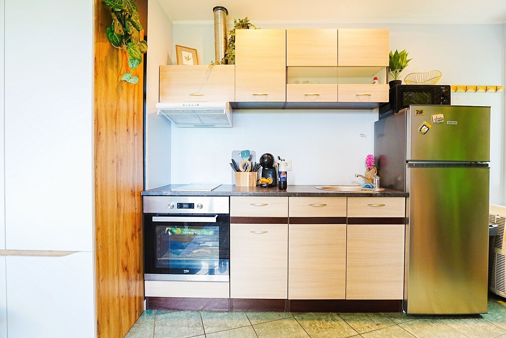 A compact kitchen with a built-in oven, a stainless steel refrigerator, and wooden cabinets.