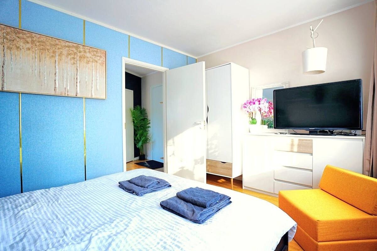 A modern hotel room with a bed, a TV, a sofa, and a plant.