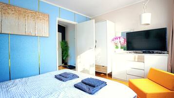 Ein modernes Hotelzimmer mit Bett, Fernseher, Sofa und einer Pflanze.