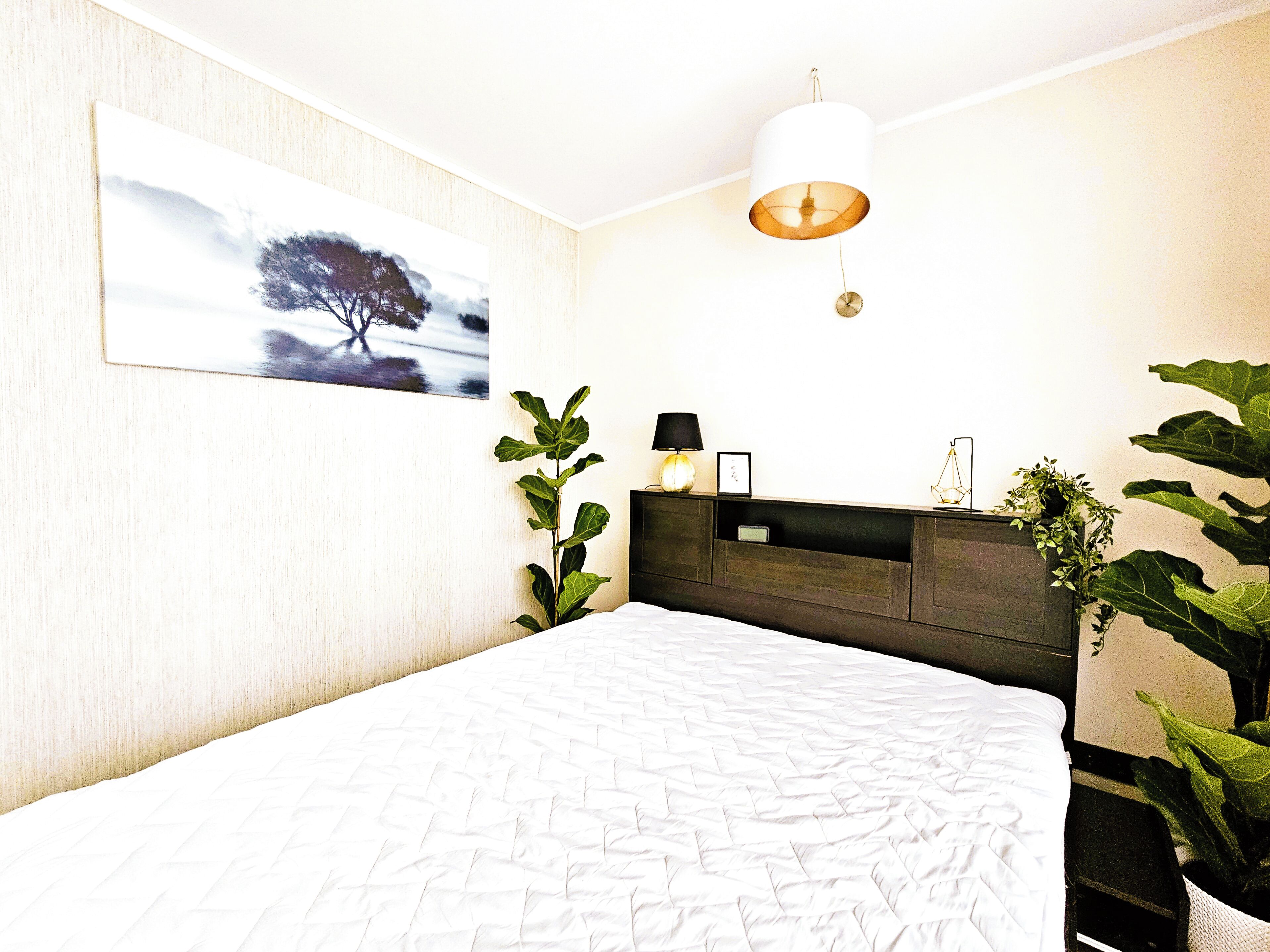 A bedroom with a bed, a nightstand, a wall-mounted lamp, and a painting.