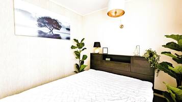 A bedroom with a bed, a nightstand, a wall-mounted lamp, and a painting.