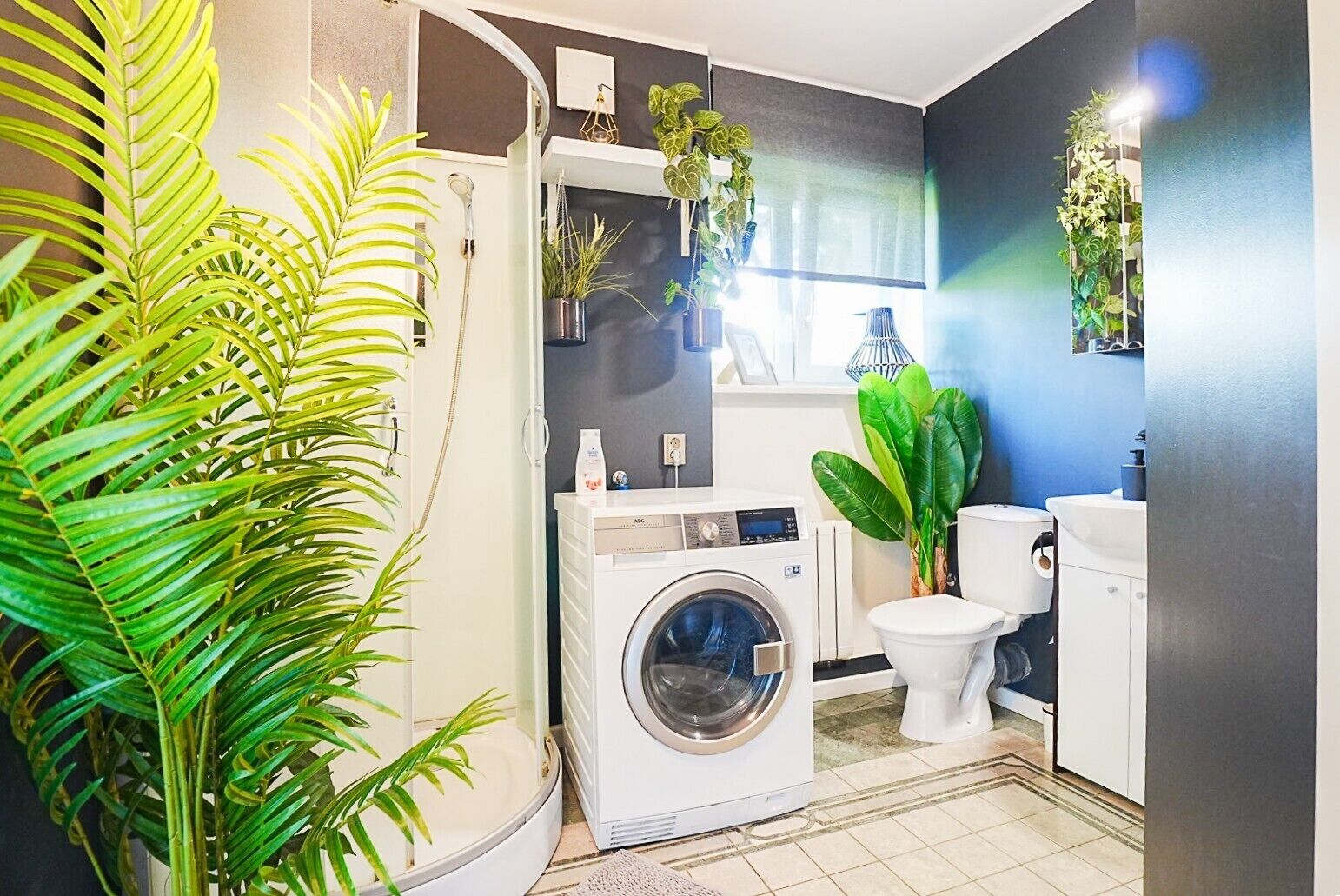 A modern bathroom with a washing machine, toilet, and potted plants.