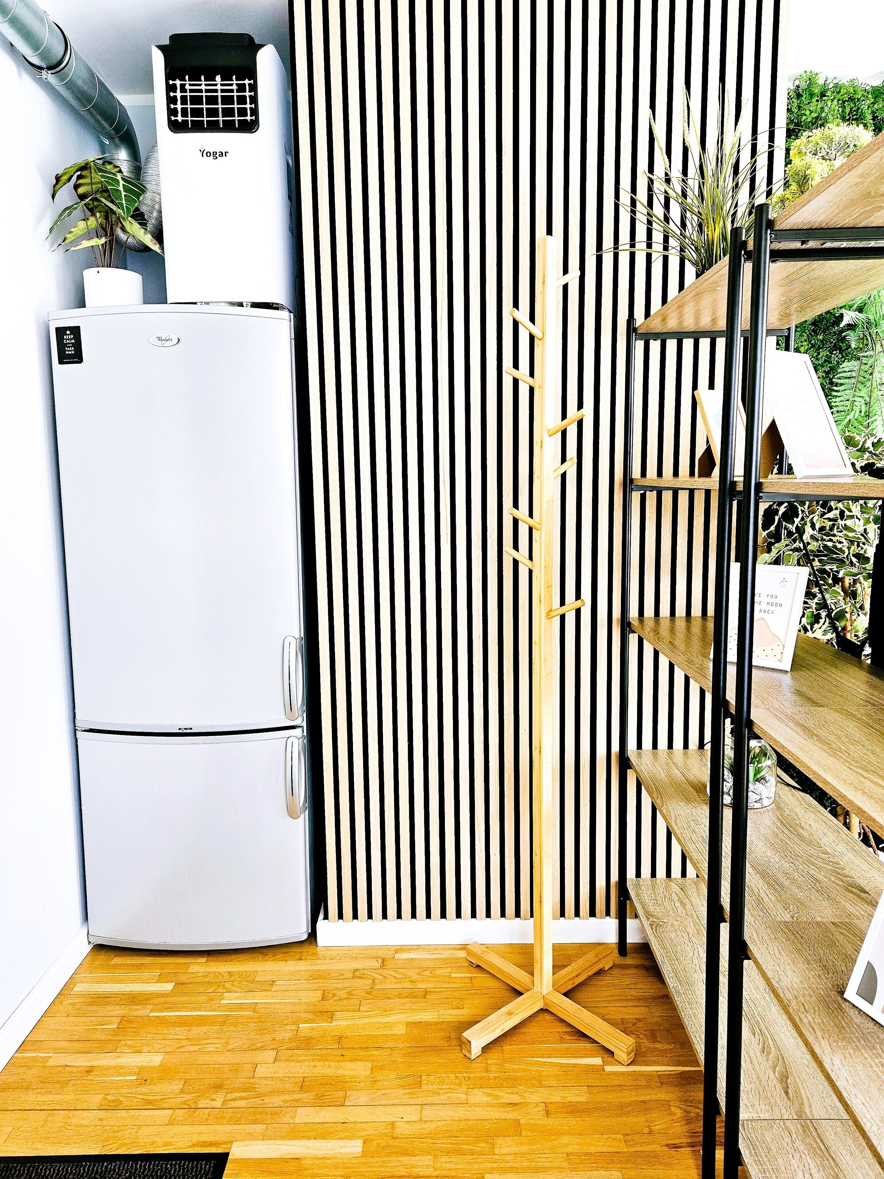 Une cuisine compacte avec un réfrigérateur blanc, un meuble en bois muni de crochets et un mur à rayures noires et blanches.