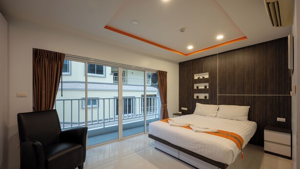 A modern hotel room with a large bed, a chair, a nightstand, and a view of a building through a sliding glass door.
