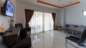 A modern living room with a flat-screen TV, a dining area with a table and chairs, and a sofa with patterned cushions.