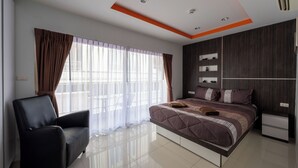 A modern bedroom with a large bed, a black armchair, a bedside table, and a window with sheer curtains.